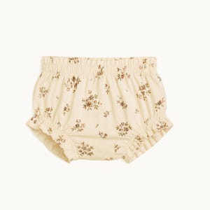 Peut inclure: Culotte bouffante pour bébé de couleur crème avec un motif floral marron répétitif. Le vêtement présente une taille élastiquée et des ouvertures de jambes à volants, offrant une silhouette froncée et ample dans des tons neutres.