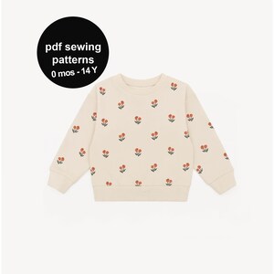 Op de afbeelding: Crèmekleurige sweatshirt versierd met een herhalend patroon van kleine rode en groene bloemmotieven. De tekst "pdf sewing patterns 0 mos - 14 Y" wordt weergegeven in een zwarte cirkel. De sweatshirt heeft een ronde hals en lange mouwen.