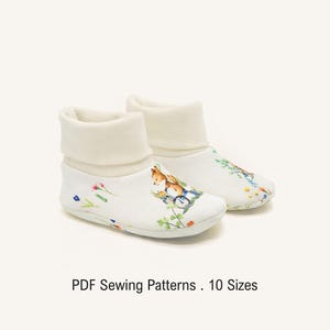 May include: A pair of white fabric baby booties featuring a colorful illustration of a small fox and floral accents. The booties have a soft, folded cuff at the top. The text below the booties reads: PDF Sewing Patterns . 10 Sizes.