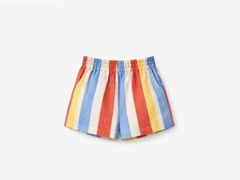 May include: Shorts featuring a vertical striped pattern in alternating colors of red, white, light blue, and yellow. The garment has an elasticized waistband with gathered fabric and two side pockets, constructed with a straight hemline.