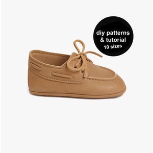 May include: A tan leather baby shoe in a boat shoe style. The shoe features a rounded toe, a lace-up fastening, and decorative stitching. A black circle with white text reads "diy patterns & tutorial 10 sizes".
