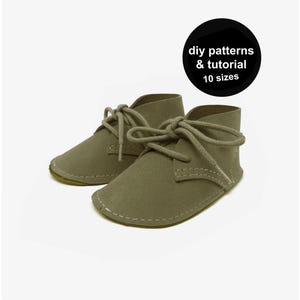 Puede incluir: Un par de botines de bebé verde oliva con cordones, sobre un fondo blanco. Los zapatos tienen una textura similar a la gamuza y están cosidos con hilo blanco. Un círculo negro en la esquina superior derecha dice "diy patterns & tutorial 10 sizes."