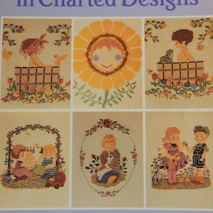 May include: A book titled "Children in Charted Designs" from the Archives of the Lindberg Press. The cover features six colorful cross-stitch designs of children.