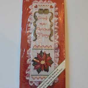 May include: A red and white counted cross stitch bookmark with a poinsettia and the text "Friends make Christmas Merry". The bookmark is packaged in a clear plastic bag with a white lace trim.