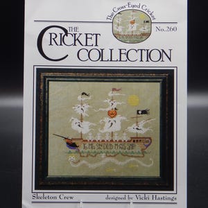 May include: A cross-stitch pattern booklet titled The Cricket Collection No. 260, Skeleton Crew, designed by Vicki Hastings. The cover features a framed embroidery of a ghost ship with skeletons, a pumpkin, and the text 16 MEN ON DEB MAS SHIP.