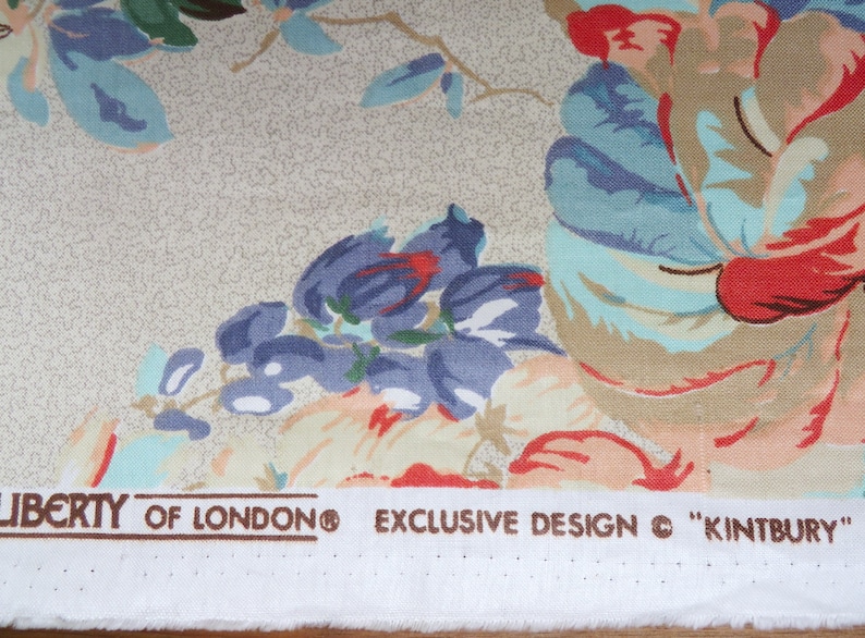 May include: Close-up of floral fabric featuring large, colourful flowers in red, blue, and peach hues against a beige backdrop. The fabric is printed with "LIBERTY OF LONDON" and "EXCLUSIVE DESIGN &copy; "KINTBURY"". Ideal for dressmaking or crafting.