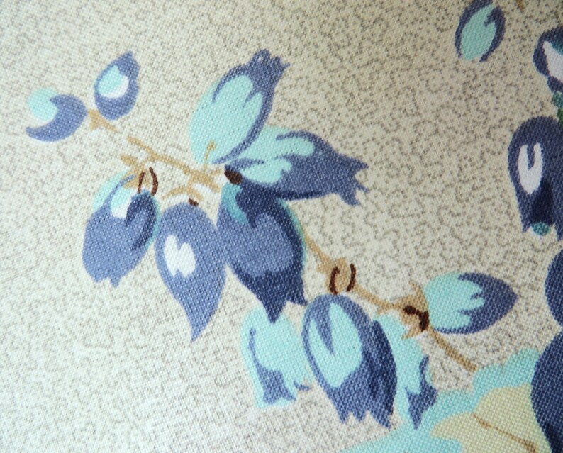 May include: Close-up of a fabric with a floral pattern. The design features blue and teal-coloured stylized flowers and leaves on a beige background. The fabric has a textured appearance, suggesting a woven material.