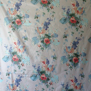 May include: Floral fabric featuring a pattern of red roses, blue and green foliage, and blue flower clusters on a light beige backdrop. The fabric has a vintage, romantic style.