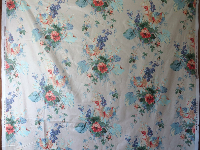 May include: Floral fabric featuring a pattern of red roses, blue and green foliage, and blue flower clusters on a light beige backdrop. The fabric has a vintage, romantic style.