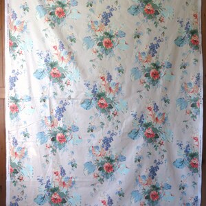 May include: A large piece of fabric with a repeating floral pattern. The design features clusters of red roses, blue and purple flowers, and large, light blue leaves on a beige background. The fabric is draped.
