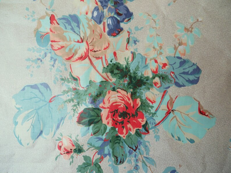 May include: A fabric featuring a floral design with large blooms and foliage. The flowers are predominantly red, pink, and peach, with blue and green leaves. The background is a pale grey with a speckled texture.