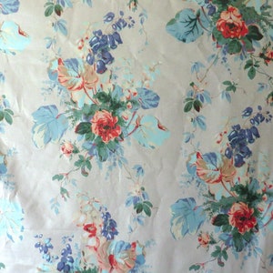 May include: A floral fabric with a pale beige backdrop. The pattern showcases clusters of red roses, blue and pale blue leaves, and purple flowers. The design is a classic, vintage style.