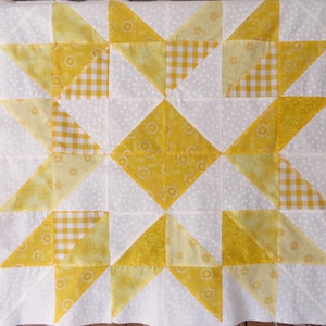 May include: A white quilt with a yellow and white star pattern. The quilt is made of squares of different fabrics, including gingham and solid yellow.