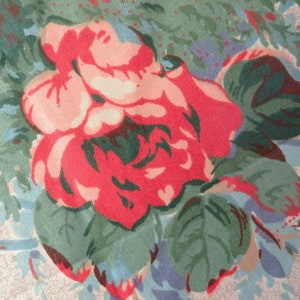 May include: Close-up of a floral fabric featuring a large, vibrant red rose with pink and peach accents. The rose is surrounded by green leaves and a background of light blue and beige tones, creating a vintage aesthetic.