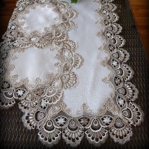 May include: A white table runner with a lace border in a beige and white pattern. The runner has a matching round placemat.