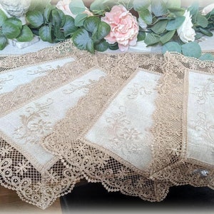 May include: Set of five beige lace placemats with embroidered floral designs. The placemats have a delicate lace border and are perfect for adding a touch of elegance to any table setting.