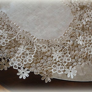 May include: A beige table runner with a white lace trim featuring a floral design. The lace trim has a scalloped edge.