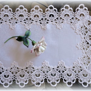 May include: White lace table runner with a delicate floral design. The runner has a scalloped edge and is perfect for adding a touch of elegance to any table setting.