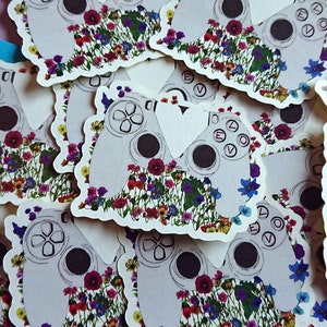 Könnte beinhalten: Nahaufnahme eines Stapels weißer Videospiel-Controller-Aufkleber. Die Controller sind von einem bunten Blumendesign umgeben.