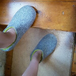 May include: A pair of gray wool slippers with a lime green trim. The slippers are worn on a person's feet.