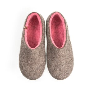May include: A pair of gray felt slippers with pink felt lining. The slippers have a rounded toe and a flat sole.