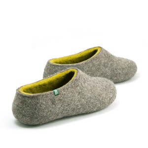 May include: A pair of gray felt slippers with a bright yellow lining. The slippers have a rounded toe and a simple design.