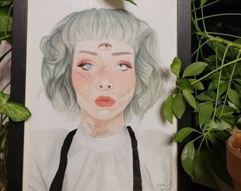 May include: A framed drawing of a person with green hair and a third eye. The person is wearing a white shirt with a black collar and a black strap. The drawing is on a white background.