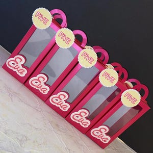 May include: Five pink gift bags with clear windows and handles are arranged diagonally. Each bag has the name "Eva" in a cursive font and a yellow circle sticker that says "FIVE". The bags are on a marble surface.