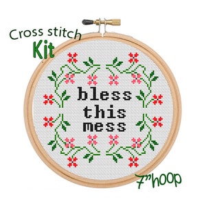May include: Cross stitch kit with a 7-inch hoop featuring a white fabric with a black phrase "bless this mess" surrounded by green vines and pink flowers.