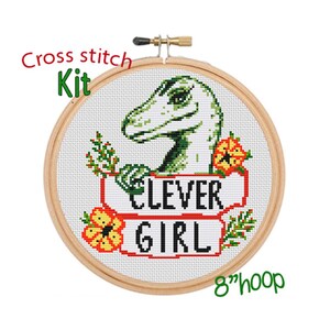 May include: Cross stitch kit featuring a green dinosaur with the text "Clever Girl" in red and white on a banner with yellow flowers. The kit comes with an 8-inch hoop.