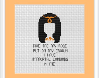 Puede incluir: Patrón de punto de cruz con una ilustración en negro y naranja de una mujer con una corona y el texto "Give me my robe put on my crown I have immortal longings in me."