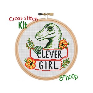 May include: Cross stitch kit featuring a green dinosaur with the text "Clever Girl" in a red and white banner. The kit includes an 8-inch hoop.