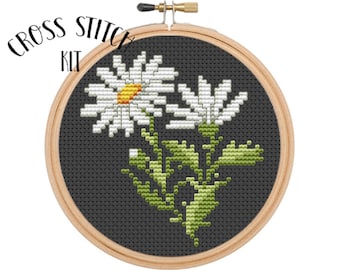 May include: Cross stitch kit featuring a white daisy flower with a yellow center on a black background. The kit includes a hoop and needle.
