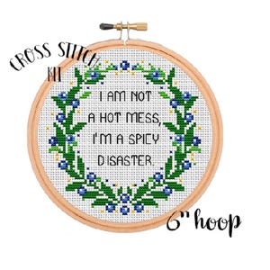 May include: Cross stitch kit featuring a wreath of green leaves and blue berries with the text "I am not a hot mess, I'm a spicy disaster." The kit is designed for a 6 inch hoop.