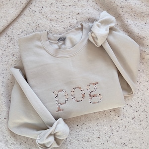 May include: A beige sweatshirt with a floral design spelling out "pog" on the front.