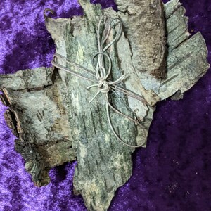 K&ouml;nnte beinhalten: Ein B&uuml;ndel Rinde, mit Schnur zusammengebunden, auf einem violetten Hintergrund. Die Rinde ist hellbraun und hat eine raue Textur.