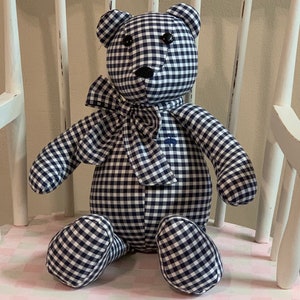May include: A black and white gingham teddy bear with black button eyes. The bear is sitting on a white chair with a pink and white checkered seat.