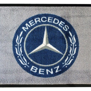 May include: A gray doormat with a blue and white Mercedes-Benz logo. The logo is a circle with the words "Mercedes" and "Benz" around a three-pointed star.