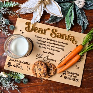 May include: A rectangular wooden serving board featuring the gold-coloured text Dear Santa, a poem, and the name The Simpsons. It includes designated areas labelled Milk & Cookies for Santa and Carrots for the Reindeer, with engraved graphics.