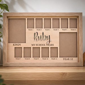 May include: A light-coloured wooden school years photo frame featuring the name Ruby in silver script. The frame includes slots labelled Kindy, Year 1 through Year 12, and the text MY SCHOOL YEARS engraved in the centre of the wooden board.