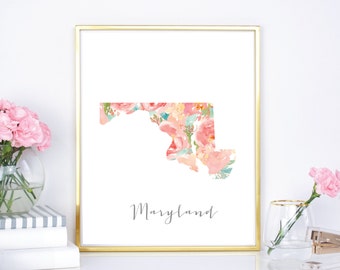 Puede incluir: Una impresión de arte imprimible con un diseño floral en tonos de rosa, melocotón y verde. El diseño tiene la forma del estado de Maryland. La impresión tiene un marco dorado y la palabra "Maryland" está escrita en cursiva debajo del diseño.