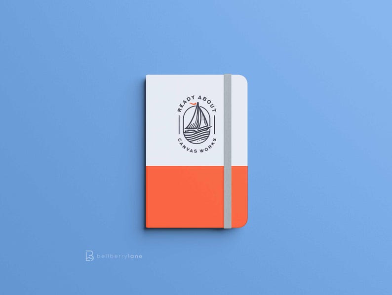 May include: A white and orange notebook with a black and white logo that says "Ready About Canvas Works" with a sailboat and a bird in the logo.