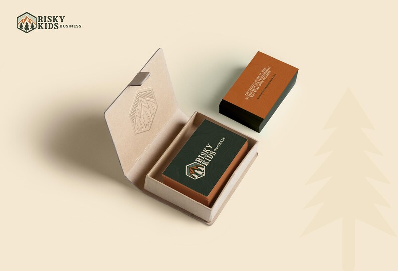 May include: A brown box with a logo for "Risky Kids Business" on the top. The box is open and a business card with the same logo is inside. The business card is on a dark green background with white text.
