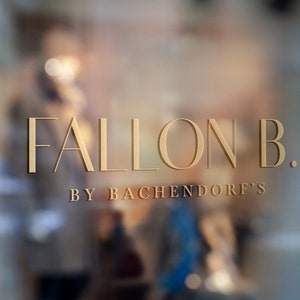 May include: Gold lettering on a glass storefront reads "FALLON B. BY BACHENDORF'S".