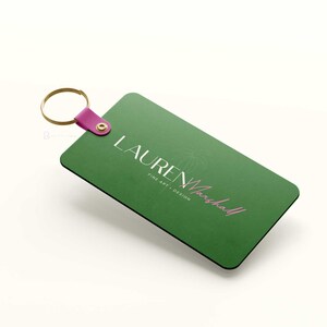 May include: Green rectangular keychain with a gold ring and a pink strap. The keychain has the text "LAUREN Marshall" in white and pink lettering with the words "FINE ART + DESIGN" in white lettering.