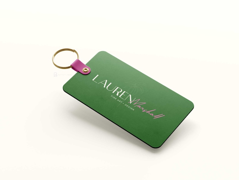 May include: Green rectangular keychain with a gold ring and a pink strap. The keychain has the text "LAUREN Marshall" in white and pink lettering with the words "FINE ART + DESIGN" in white lettering.