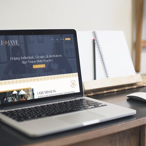 May include: A laptop computer displaying a website for a business called Elle Jaye. The website features a dark blue background with gold accents and the text "Helping Individuals, Groups, & Institutions Align Vision With Practice". The website also includes a section titled "Our Mission".