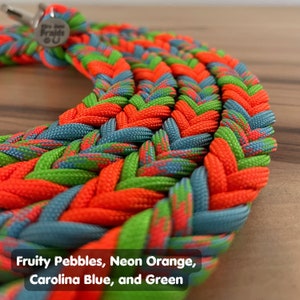 May include: Close-up of a braided dog leash in a multi-colored pattern. The leash is made of paracord and features a bright neon orange, green, Carolina blue, and a Fruity Pebbles color.