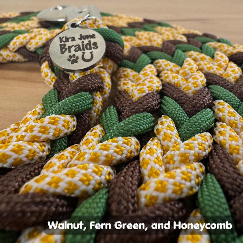 May include: A braided dog leash in walnut, fern green, and honeycomb colors. The leash has a metal tag that reads "Kira June Braids U".