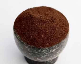 May include: A close-up of a dark brown powder in a gray and black speckled bowl. The powder is finely ground and has a smooth texture.